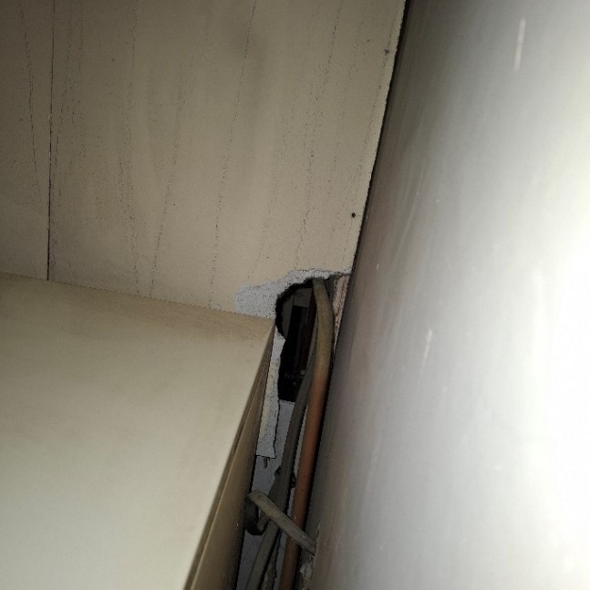 Damaged asbestos insulating board lining around a warm air heater cupboard